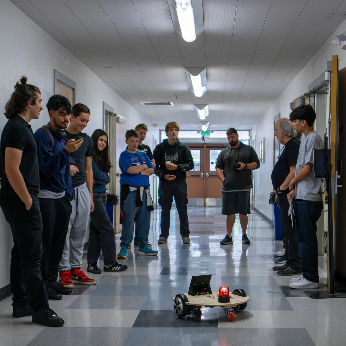 (L-R) Eren Hughes, Kevin Valdez, Kian Carrithers, Camila Rodrigues, Braeden Day, Kanam Romberger, Murphy Wright, Geovani Sorto, and Raul Castaneda from John Burroughs High School watch Return student Joshua Kubizne showcase a prototype that was built in 3 weeks. 